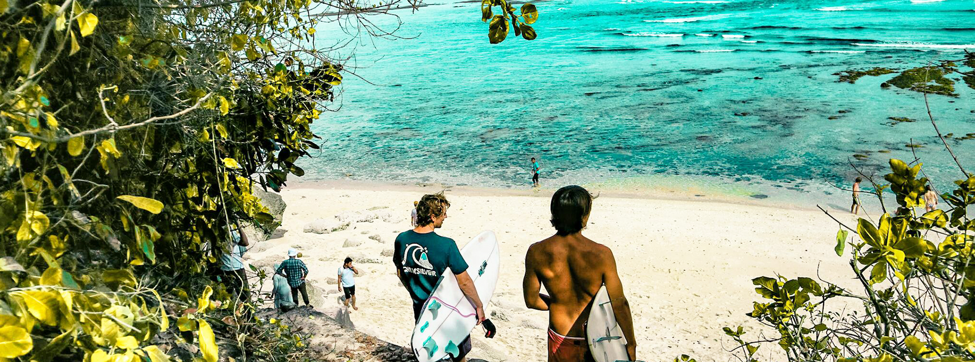 « Je pars à Bali en octobre, qui est partant ? » : Le covoyage séduit une génération en quête de liberté - L'ADN Deux surfers et plusierus personnes sur une plage balinaise