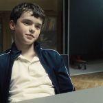 une jeune garçon assi. à une table l'air sur de lui.