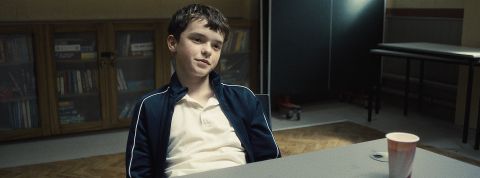 24-03-adolescence une jeune garçon assi. à une table l'air sur de lui.