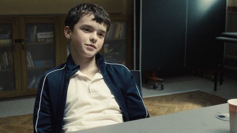 une jeune garçon assi. à une table l'air sur de lui.