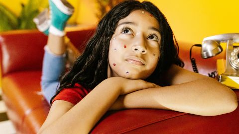 Une jeune fille sur son lit, un téléphone à ses côtés, les yeux levés vers le plafond, l'air blasé