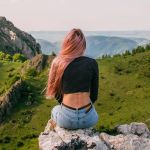 Une femme de dos aux longs cheveux roses devant un paysage montagneux