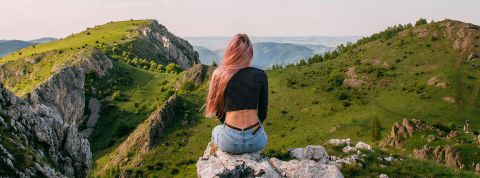 Chacun cherche son lieu… mais où se sent-on vraiment chez soi ? Une femme de dos aux longs cheveux roses devant un paysage montagneux