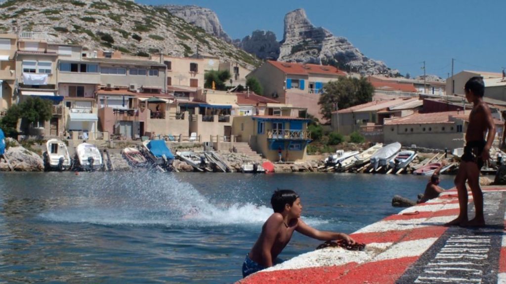 Hyper-tourisme et cartepostalisassion du littoral : bienvenue aux Goudes des enfants qui plongent dans l'eau d'un port