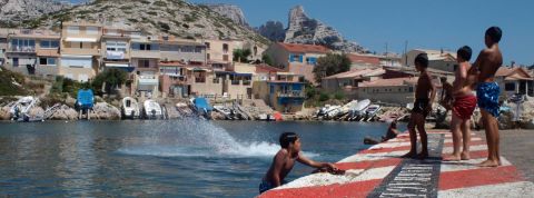 Hyper-tourisme et cartepostalisassion du littoral : bienvenue aux Goudes des enfants qui plongent dans l'eau d'un port
