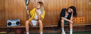 Deux filles sur un banc de sport en bois, l'une portant une coupe, l'autre dépitée