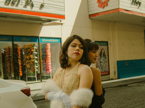 Deux filles en robes vintage dos à dos devant un cinéma à l'ancienne