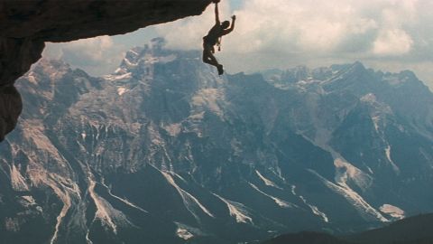 Un homme suspendu dans le vide, accroché à la montagne (image du film Cliffhanger)