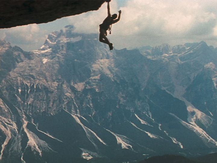 Un homme suspendu dans le vide, accroché à la montagne (image du film Cliffhanger)