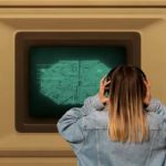 Une ado de dos en veste en jean et casque devant un ordinateur géant