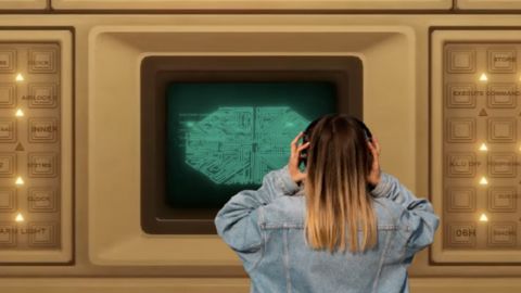 Une ado de dos en veste en jean et casque devant un ordinateur géant