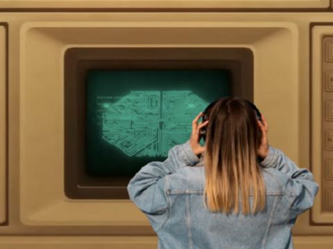 Une ado de dos en veste en jean et casque devant un ordinateur géant