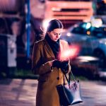 Une femme regarde son telephone dans la rue en soirée