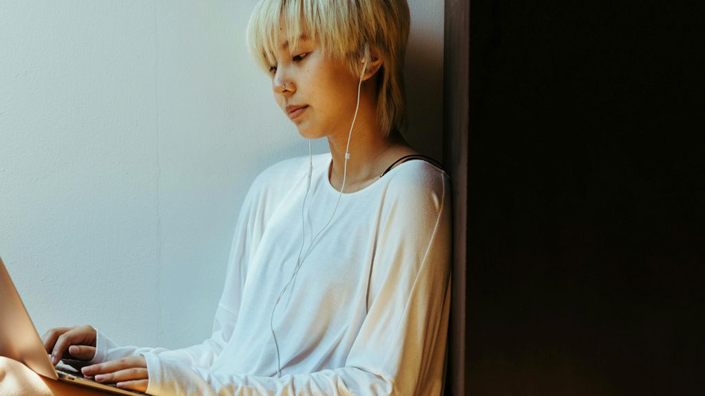 Une jeune femme asiatique avec écouteurs regarde son ordinateur portable