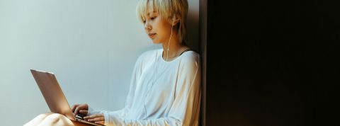 Une jeune femme asiatique avec écouteurs regarde son ordinateur portable