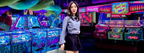 Newtro, nos vies entre IRL et mondes numériques Une jeune asiatique avec une tenue d'écolière modernisée dans une salle de jeux d'arcade