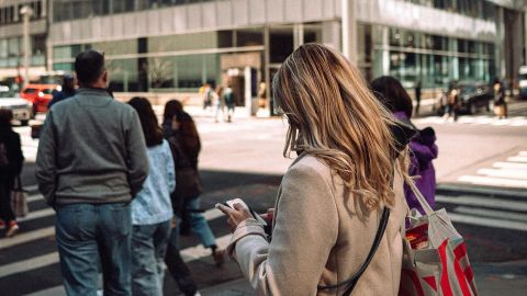 Une femme blonde de dos les yeux rivés sur son smartphone au passage piéton
