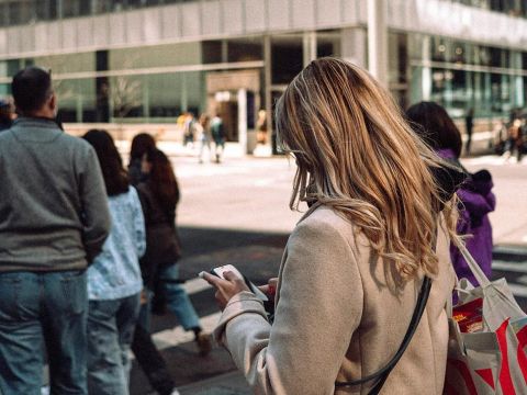 Une femme blonde de dos les yeux rivés sur son smartphone au passage piéton