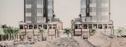 Deux immeubles modernes au Koweit derière des monceaux de sable et des palmiers