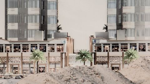 Deux immeubles modernes au Koweit derière des monceaux de sable et des palmiers