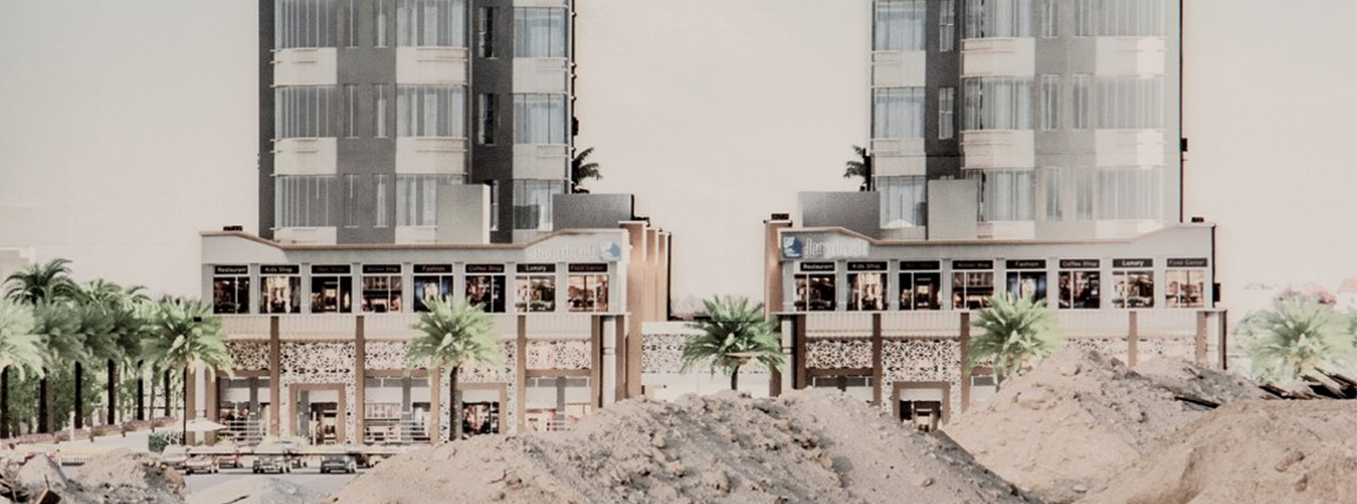 Deux immeubles modernes au Koweit derière des monceaux de sable et des palmiers