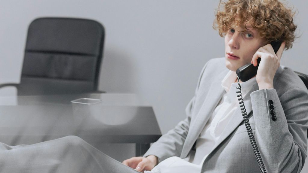 Un jeune homme les pieds sur son bureau dans un univers gris