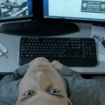 Un homme tête en arrière devant deux écrans d'ordinateurs