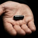 une main qui tend une pilule noire