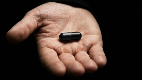 une main qui tend une pilule noire