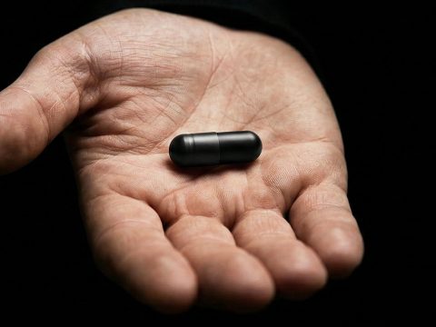 une main qui tend une pilule noire