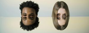 Un jeune homme à la peau mate, métis, et une jeune femme blonde avec les reflets du haut de leur visage dans un miroir horizontal