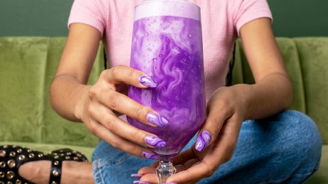 Une fille sur un canapé vert matcha tient un latte Ube de couleur violette