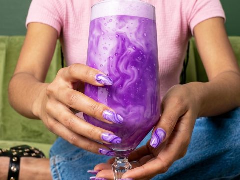 Une fille sur un canapé vert matcha tient un latte Ube de couleur violette