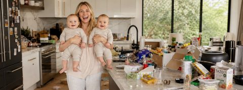 Chaussettes dépareillées et fin des activités périscolaires : les mamans tigres laissent la place aux « beta mums » Une jeune maman souriante avec ses jumeaux dans les bras riant, dans une cuisine en bazar