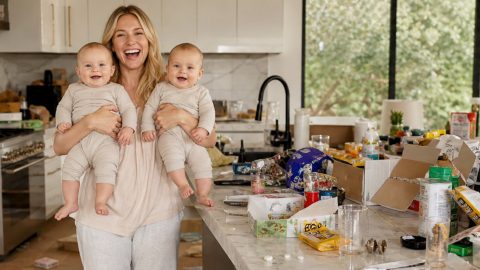 Une jeune maman souriante avec ses jumeaux dans les bras riant, dans une cuisine en bazar