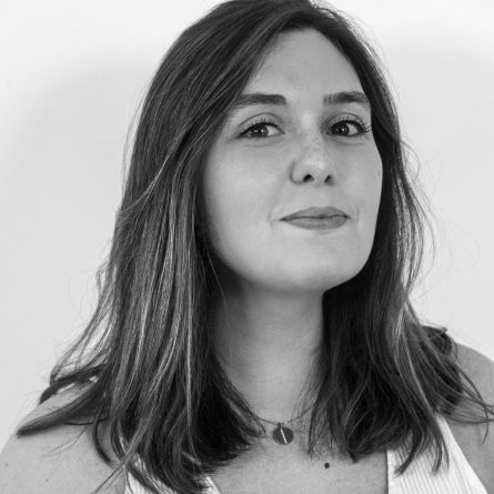 Close-up black-and-white portrait of a woman with shoulder-length hair, a subtle smile, wearing a white top and a small pendant necklace.