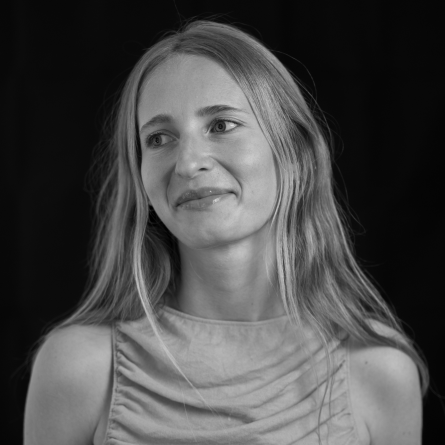 Black-and-white portrait of a smiling woman with long hair, looking slightly to the left, from the shoulders up against a dark background.