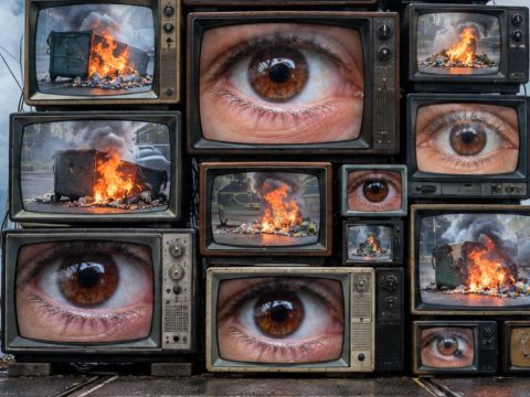 Stacked vintage TVs showing close-up brown eyes, with a hazy protest and flames in the background, conveying media saturation of unrest.